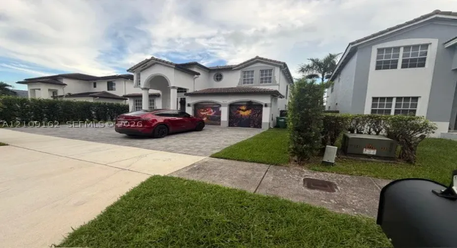 Two-story residence featuring a stucco facade, arched entryway, multi-car garage, and paved driveway