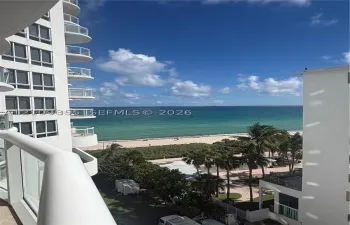 Elevated balcony featuring glass railings and direct oceanfront scenery, accompanied by high-rise architectural elements