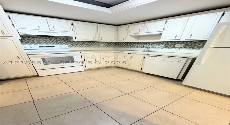 Kitchen featuring white cabinetry, mosaic tile backsplash, solid-surface countertops, tile flooring, and integrated white appliances