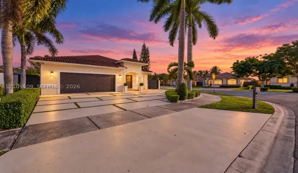 Stucco exterior residence with a multi-piece tile roof, featuring a grid-pattern concrete driveway with grass insets, mature palm trees, and manicured landscaping