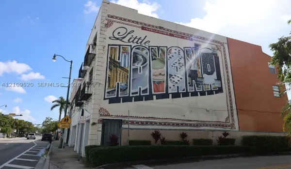 Multi-story stucco exterior featuring a large-scale mural, decorative wrought iron balconies, and manicured perimeter landscaping
