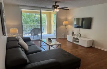 Living area featuring wood-finish flooring, ceiling fan with light fixture, and sliding glass door opening to a private balcony