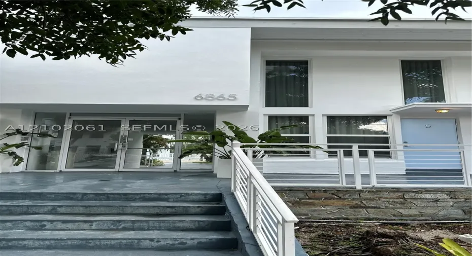 Modern building facade featuring large windows, a white railing, stone accents, and an entrance with glass​​‌​​​​‌​​‌‌​‌‌​​​‌‌​‌​‌​‌​​​‌​​ doors