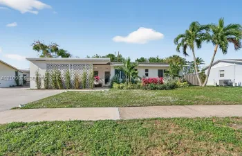 Single-story residence featuring a flat roofline, decorative lattice screen, concrete driveway, and mature palm trees