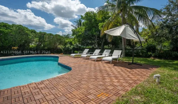Swimming pool with a curved edge, finished with modular wood-style deck tiles, surrounded by a lawn and mature perimeter landscaping