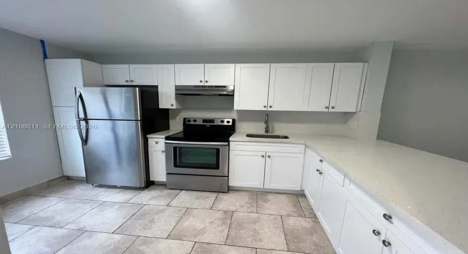 Kitchen featuring white cabinetry, solid surface countertops, stainless steel appliances, a stainless steel range hood, and tile flooring