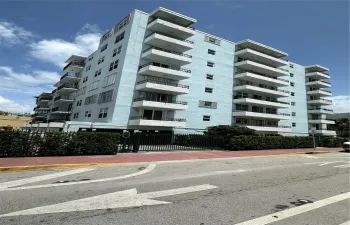 Multi-story residential building featuring a light blue stucco exterior, stacked private balconies with black metal railings, and a gated ground-level parking entrance