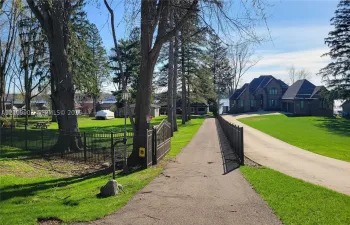 Expansive grounds featuring a multi-gabled brick exterior, paved driveway, mature trees, and decorative metal perimeter fencing