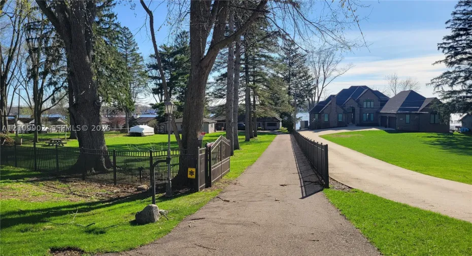 Expansive grounds featuring a multi-gabled brick exterior, paved driveway, mature trees, and decorative metal perimeter fencing