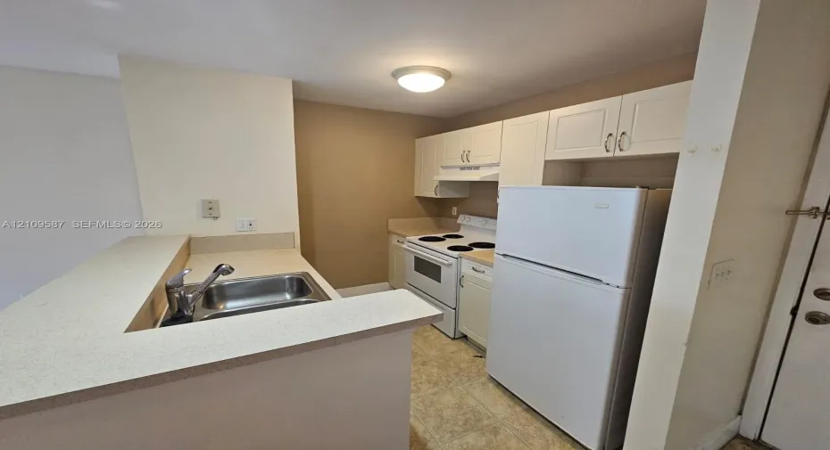 Kitchen featuring white shaker-style cabinetry, solid-surface countertops, a dual-basin stainless steel sink with a high-arch faucet, and an electric range