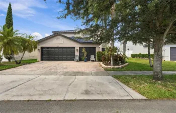 Multi-level exterior featuring a metal roof, paver driveway, three-car garage with dark-finish doors, and landscaped garden beds