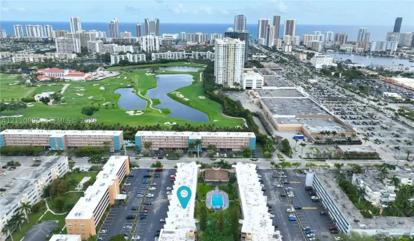 Aerial perspective of a multi-unit property featuring a central swimming pool, paved surface parking, and proximity to a golf course
