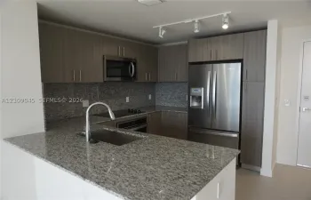 Kitchen featuring stone countertops, flat-panel cabinetry, stainless steel appliances, a single-basin undermount sink, and track lighting