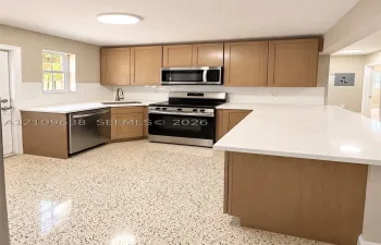 Kitchen featuring light-finish cabinetry, white solid-surface countertops, a full-height tile backsplash, stainless steel appliances, and polished speckled flooring