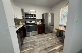 Kitchen featuring two-tone cabinetry, stainless steel appliances, wood-finish flooring, and horizontal blinds