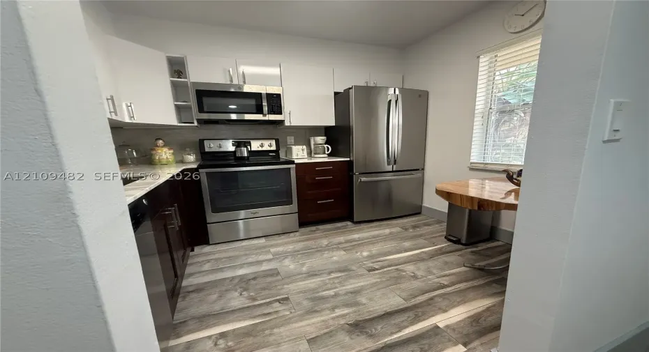 Kitchen featuring two-tone cabinetry, stainless steel appliances, wood-finish flooring, and horizontal blinds