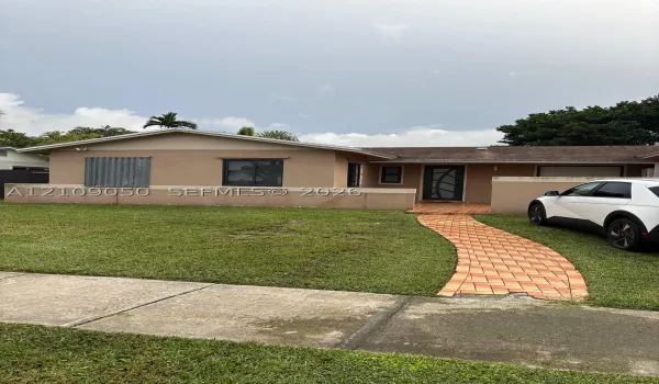 Single-story residence featuring a tan stucco exterior, decorative front door with glass inlay, masonry perimeter wall, and a curved paver walkway