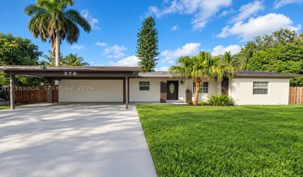 Single-story exterior featuring a concrete driveway, attached carport, smooth-stucco facade, and mature landscaping