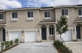 Multi-unit exterior featuring a neutral stucco facade, arched covered entryways with decorative columns, multi-panel garage doors, and grid-pattern window panes