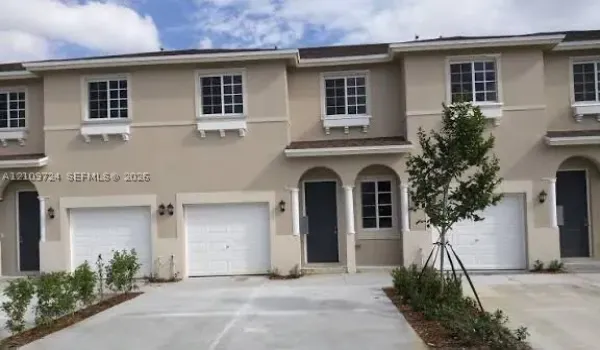 Multi-unit exterior featuring a neutral stucco facade, arched covered entryways with decorative columns, multi-panel garage doors, and grid-pattern window panes