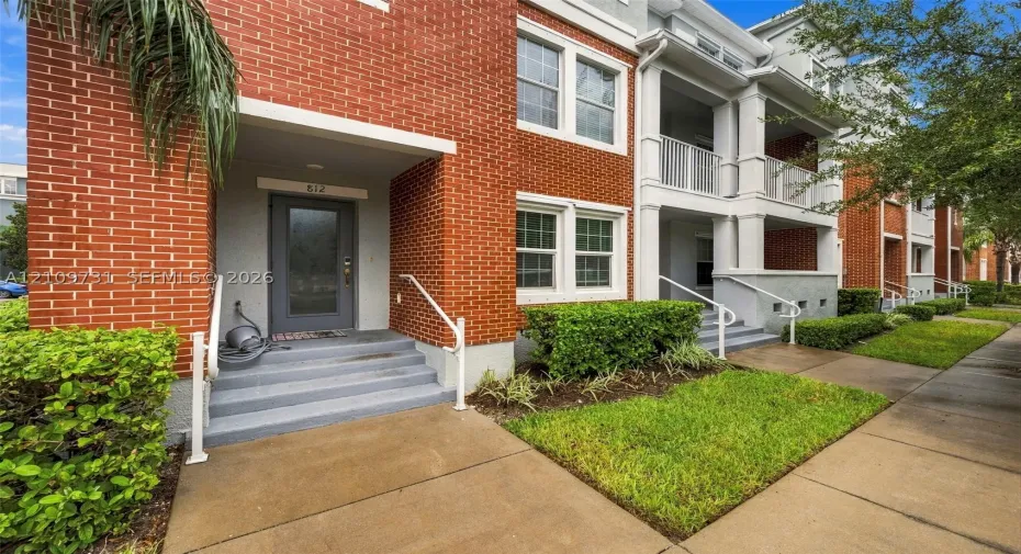 Multi-story residential exterior featuring red brick masonry, white metal railings, recessed entryways, and covered balconies