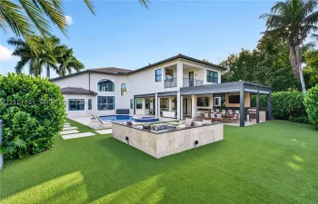 Rear exterior featuring a swimming pool, integrated spa, covered patio with outdoor kitchen, and stone-clad fire feature
