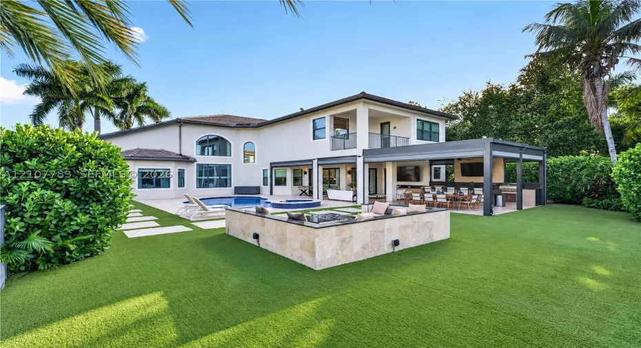 Rear exterior featuring a swimming pool, integrated spa, covered patio with outdoor kitchen, and stone-clad fire feature