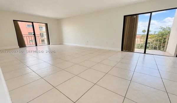 Open-concept living space featuring large-format ceramic tile flooring, neutral wall tones, and two sets of sliding glass doors providing access to exterior balconies