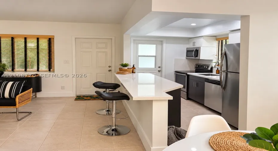 Kitchen featuring a breakfast bar with a solid surface countertop, stainless steel appliances, dark cabinetry, and tile flooring
