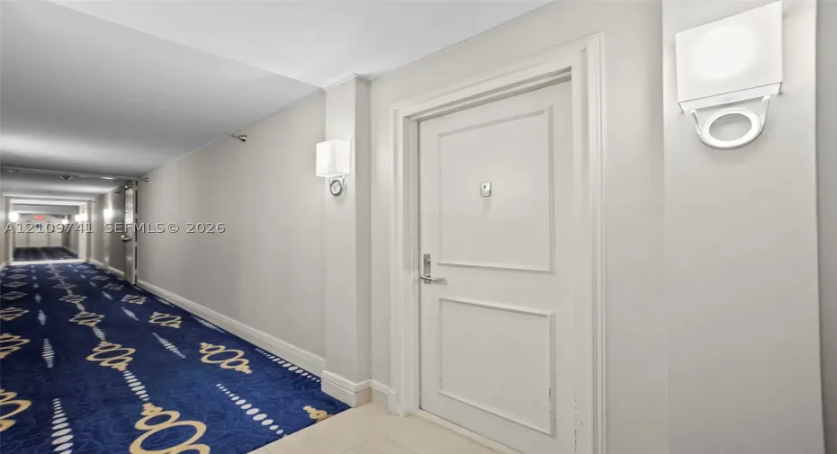Hallway featuring patterned carpet flooring, white paneled interior doors, and modern wall-mounted light fixtures