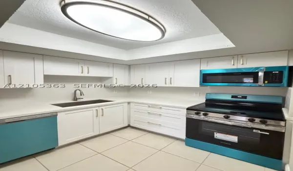 White shaker-style cabinetry with gold-tone hardware, white countertops, stainless steel sink with gooseneck faucet, tile flooring, and a recessed ceiling light fixture