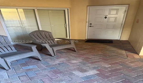 Private patio with herringbone-patterned brick pavers, sliding glass door, and solid-core paneled entry door