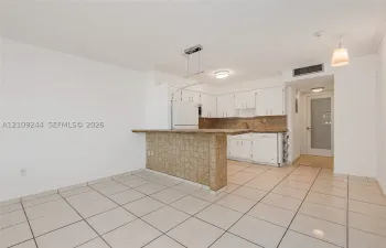 Kitchen featuring a tiled breakfast bar, white cabinetry, integrated appliances, and neutral tile flooring
