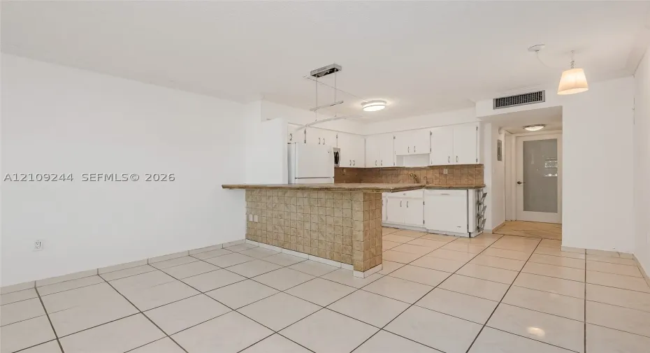 Kitchen featuring a tiled breakfast bar, white cabinetry, integrated appliances, and neutral tile flooring