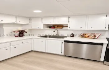 Kitchen featuring white cabinetry, solid-surface countertops, stainless steel undermount sink with arched faucet, stainless steel dishwasher, and wood-finish flooring