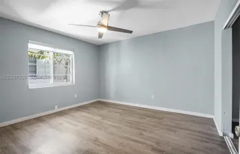Room featuring wood-finish flooring, light-toned wall paint, a sliding glass window, and a ceiling-mounted light fixture with fan blades