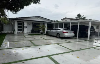 Exterior featuring a paver driveway with turf accents, a covered carport, and a white privacy gate