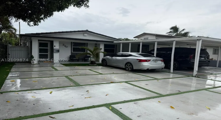 Exterior featuring a paver driveway with turf accents, a covered carport, and a white privacy gate