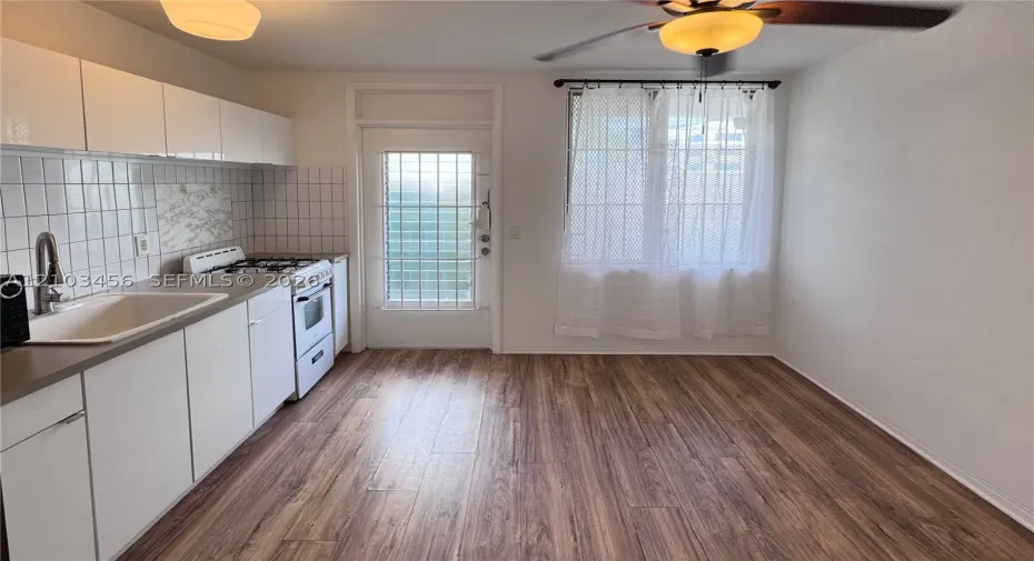 Kitchen featuring white cabinetry, wood-finish flooring, square tile backsplash, built-in gas range, and a ceiling fan with integrated lighting