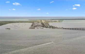 Aerial perspective of coastal landscape featuring expansive open water, a bridge, and a land-based thoroughfare