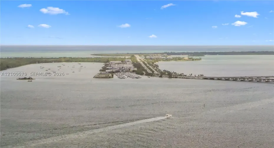 Aerial perspective of coastal landscape featuring expansive open water, a bridge, and a land-based thoroughfare