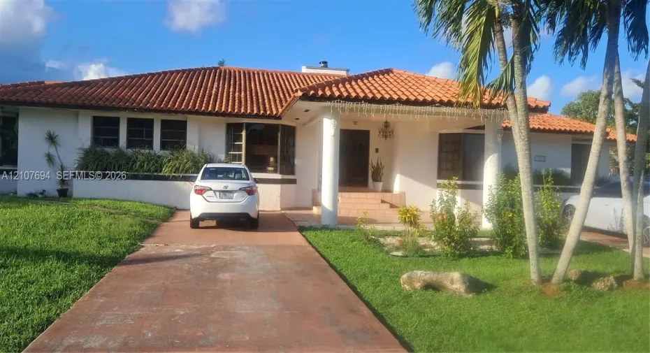 Single-story exterior featuring a red tile roof, covered entryway with structural columns, and a paved driveway