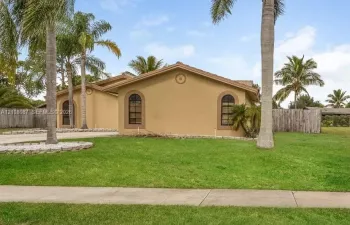 Stucco exterior featuring arched windows, decorative circular gable accents, a concrete driveway, and mature palm trees