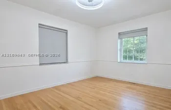 Neutral-toned room featuring wood-finish flooring, white walls with chair rail molding, multi-pane windows, and a central ceiling fixture