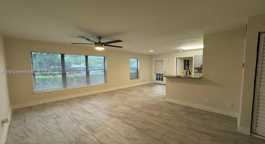 Open interior featuring ceramic tile flooring, large multi-pane windows, a central ceiling fan with integrated lighting, and a kitchen pass-through counter