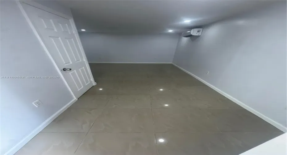 Interior space featuring neutral-tone ceramic tile flooring, recessed ceiling lighting, a wall-mounted ductless air conditioning unit, and a six-panel door