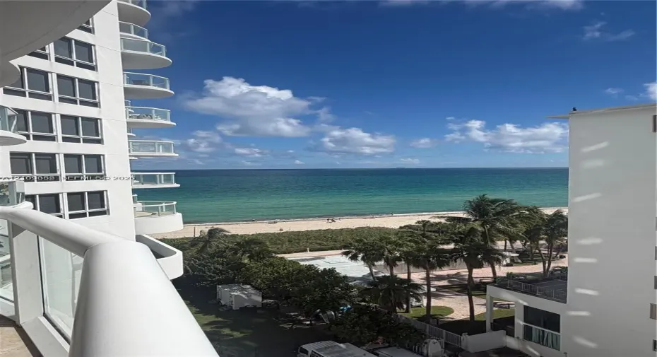 Elevated balcony featuring glass railings and direct oceanfront scenery, accompanied by high-rise architectural elements