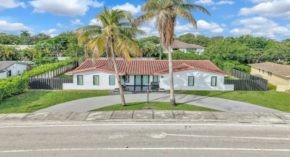Single-story exterior featuring a terracotta tile roof, white stucco facade, semicircular concrete driveway, and vertical panel fencing