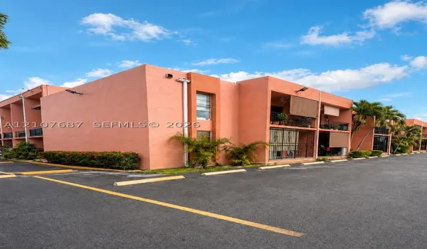 Stucco exterior building featuring covered balconies, recessed lighting, and asphalt parking area