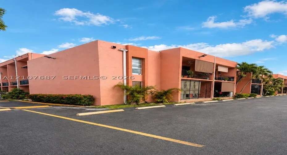 Stucco exterior building featuring covered balconies, recessed lighting, and asphalt parking area
